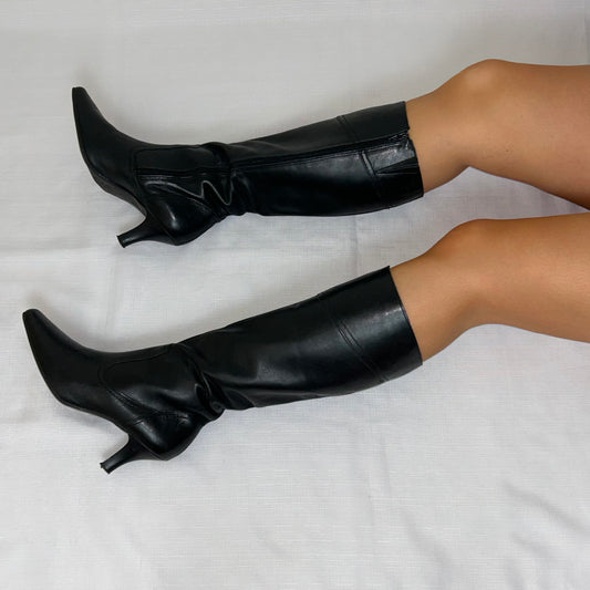 black knee high leather boots shown on a models legs laid on a white background