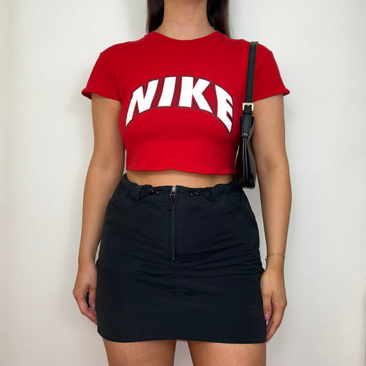 red short sleeve crop top with white nike logo shown on a model wearing a black skirt and black shoulder bag