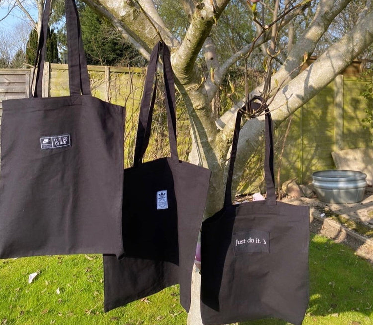 three black tote bags on a tree with grass in the background