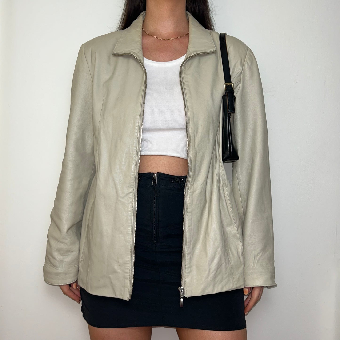 beige leather zip up jacket shown on a model wearing a white crop top and black skirt with a black shoulder bag
