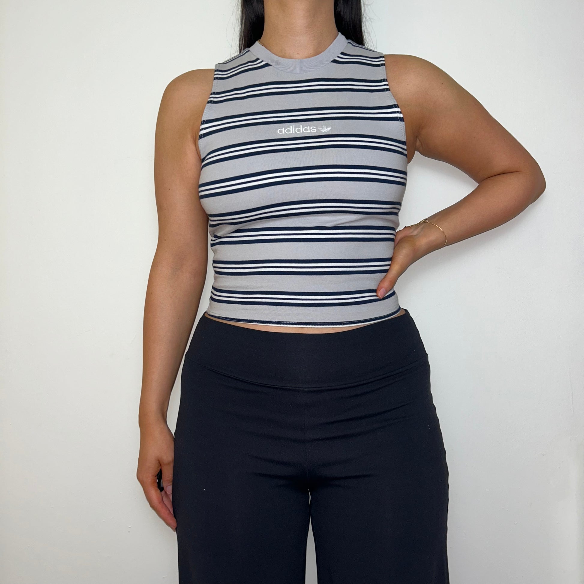 grey stripe sleeveless crop top with white adidas logo shown on a model wearing black trousers