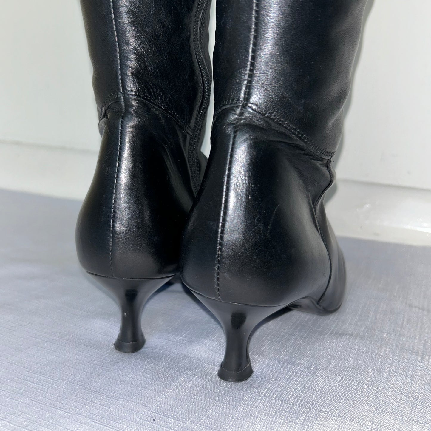 heels of black knee high kitten heel leather boots shown on a white background