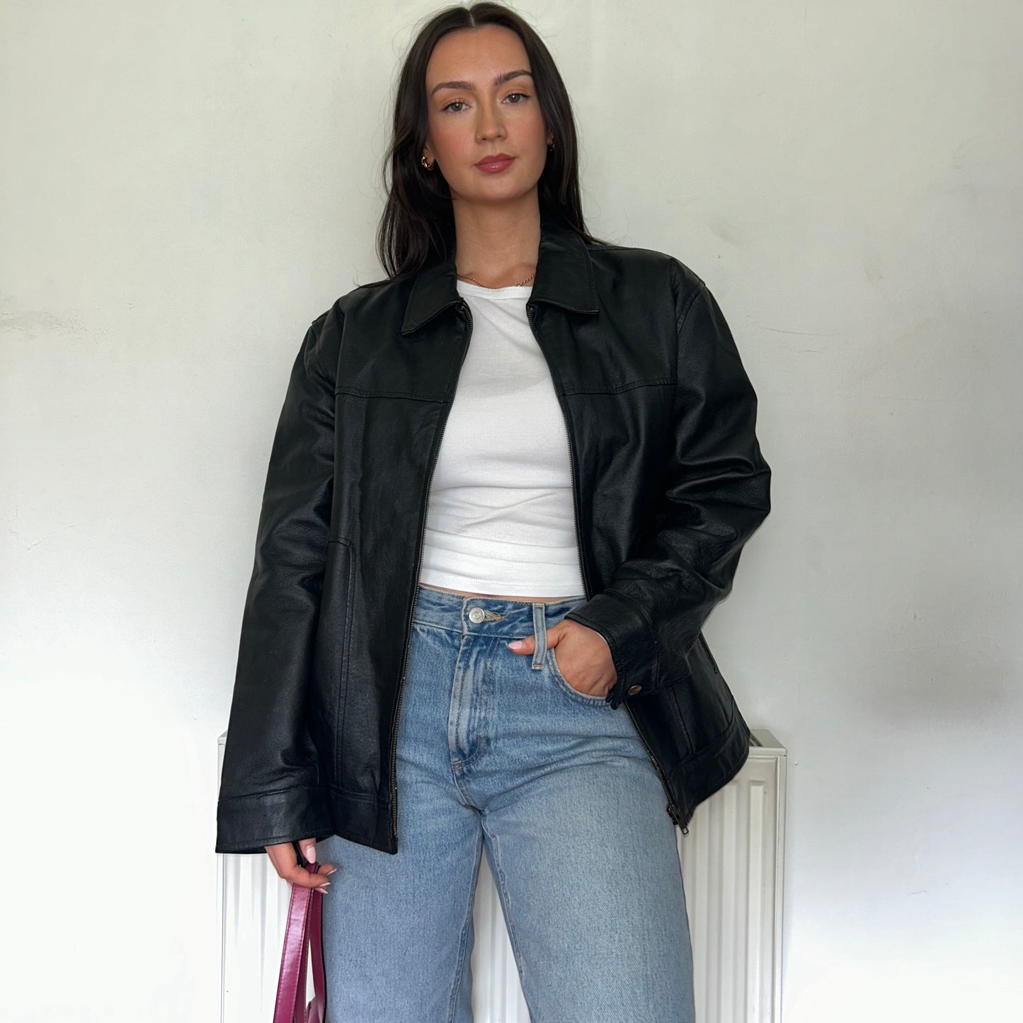 black leather vintage bomber jacket shown on a model wearing a white top and blue jeans 
