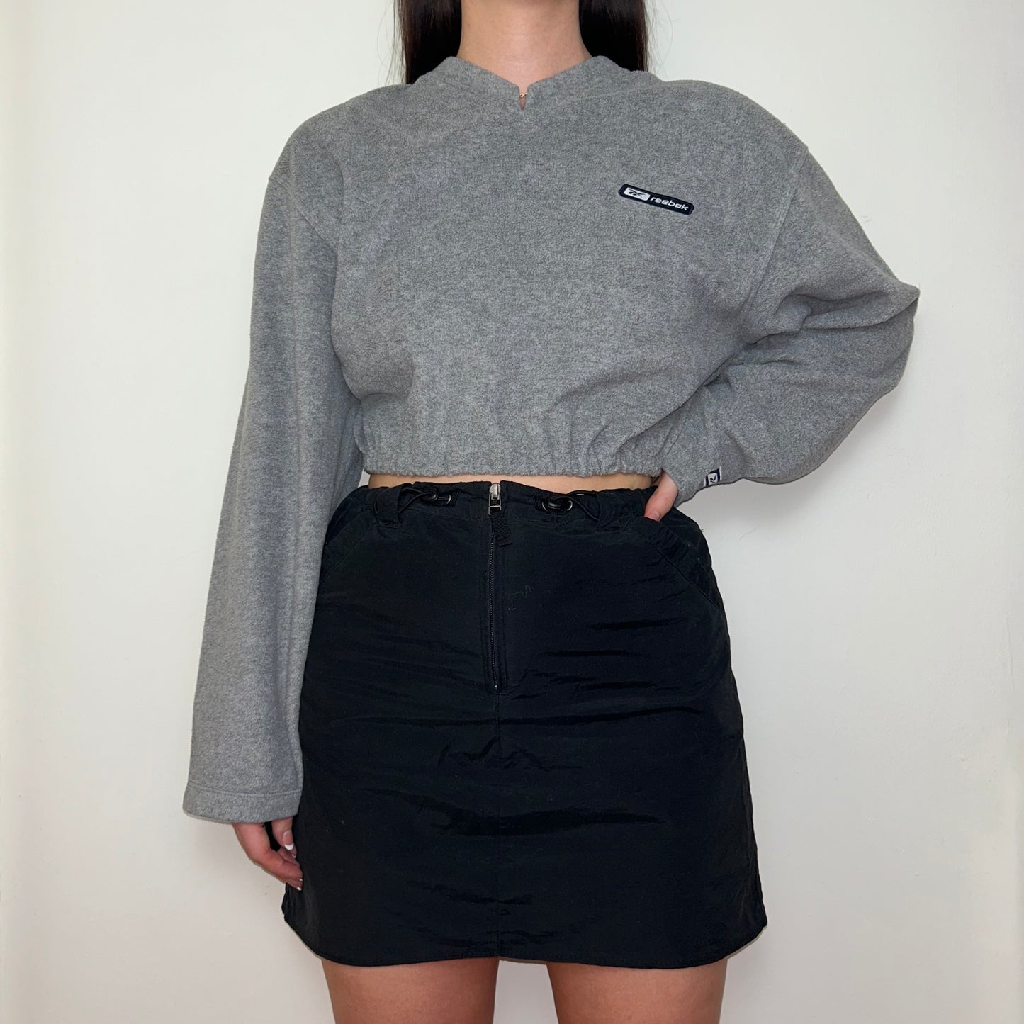 grey cropped sweatshirt with reebok logo shown on a model wearing a black skirt