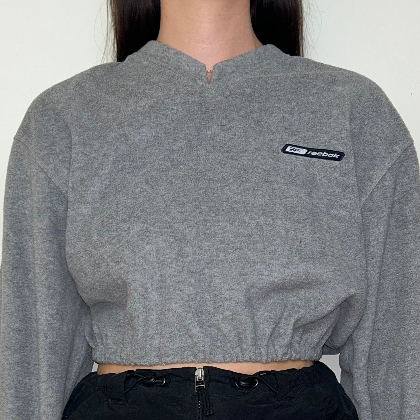 close up of grey cropped sweatshirt with reebok logo shown on a model wearing a black skirt