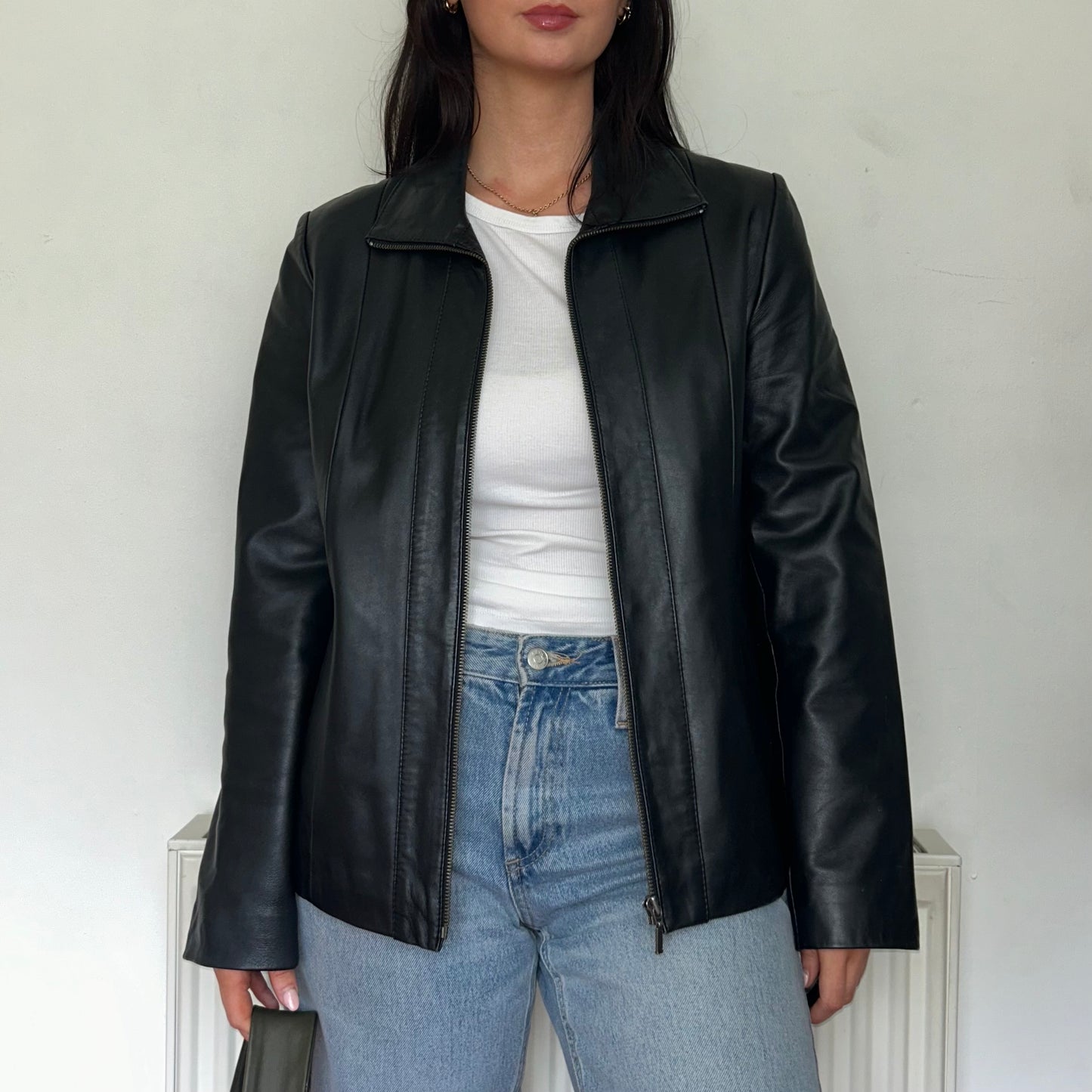 close up of black leather bomber jacket shown on a model wearing a white top and blue jeans