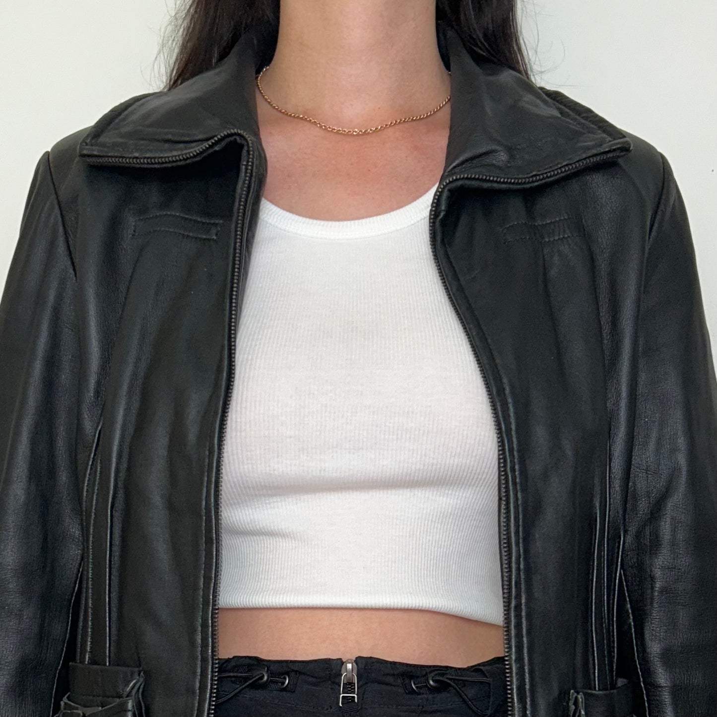 close up of black real leather jacket shown on a model wearing a white crop top and black mini skirt