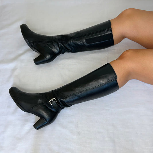 black knee high silver buckle boots shown  on a models legs laid on a white background
