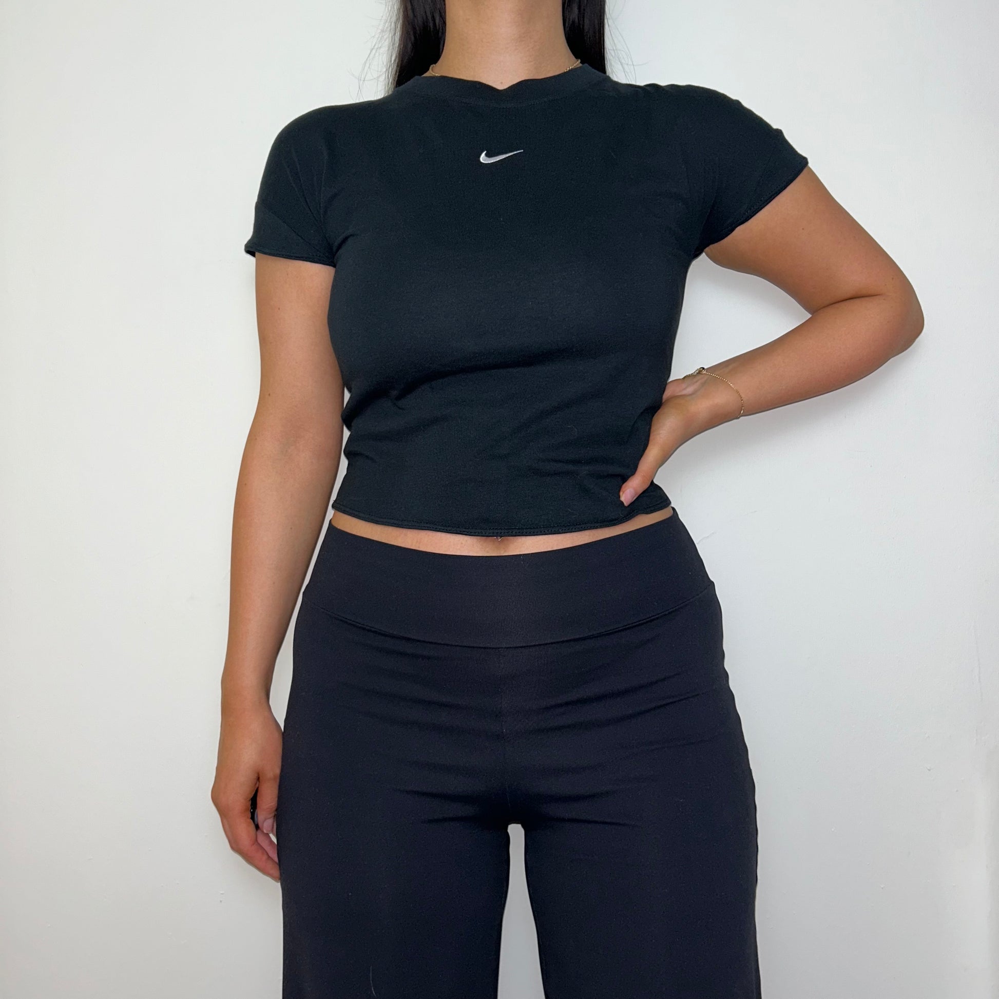 black short sleeve crop top with white nike swoosh logo shown on a model wearing black trousers
