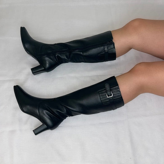 black knee high buckle boots shown on a models legs laid on a white background