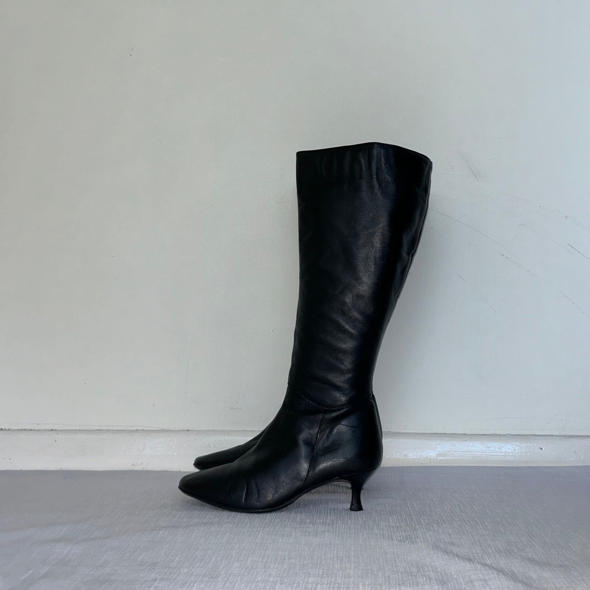 black knee high kitten heel leather boots shown on a white background