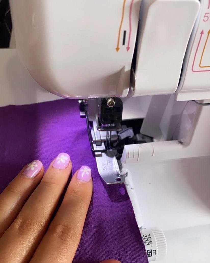 close up of sewing machine needle point with purple material going through it with a models hand on top with purple flower nails