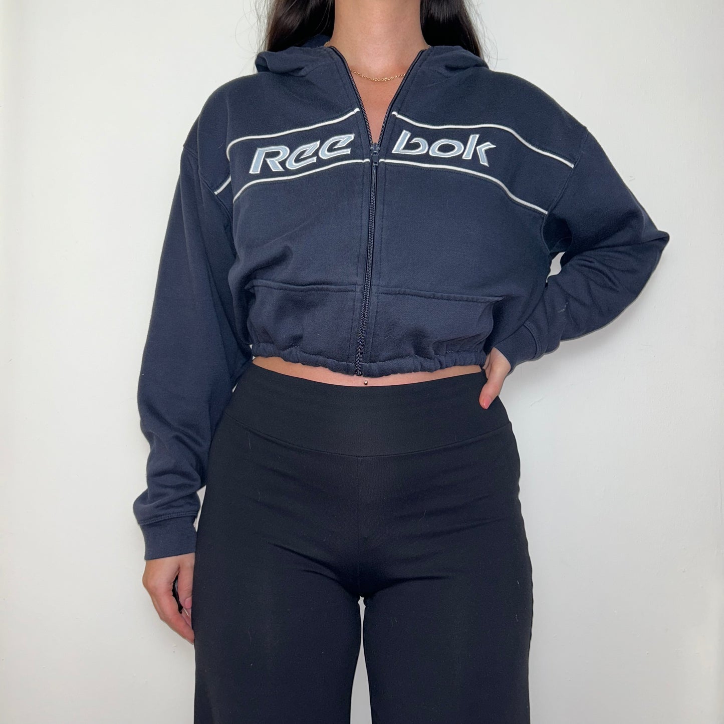 navy cropped hoodie with white reebok logo shown on a model wearing black trousers