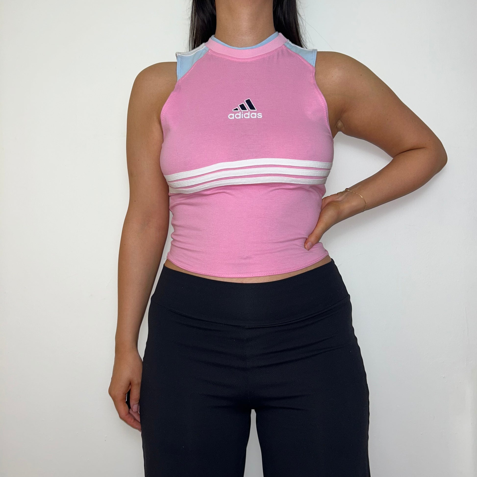 pink sleeveless crop top with black and white adidas logo shown on a model wearing black trousers