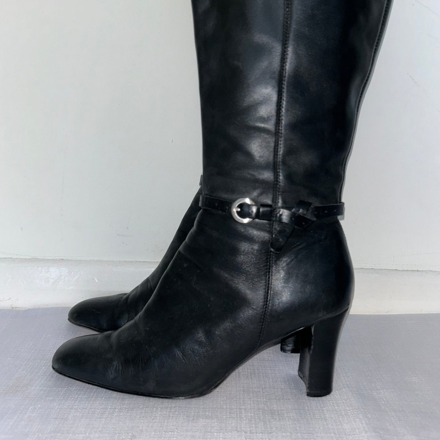 close up of black knee high leather buckle boots on a white background