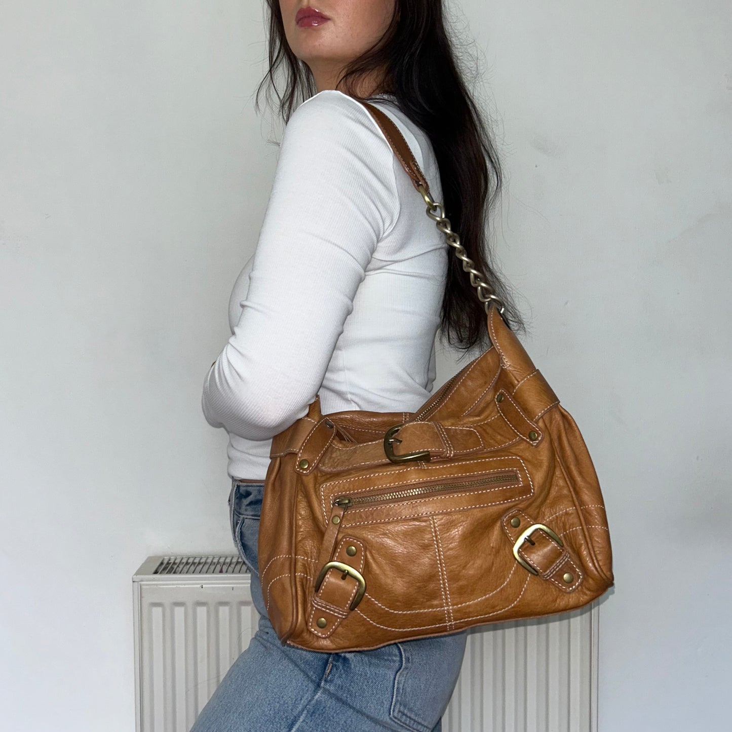 tan brown leather shoulder bag shown on a models shoulder wearing a white top and blue jeans