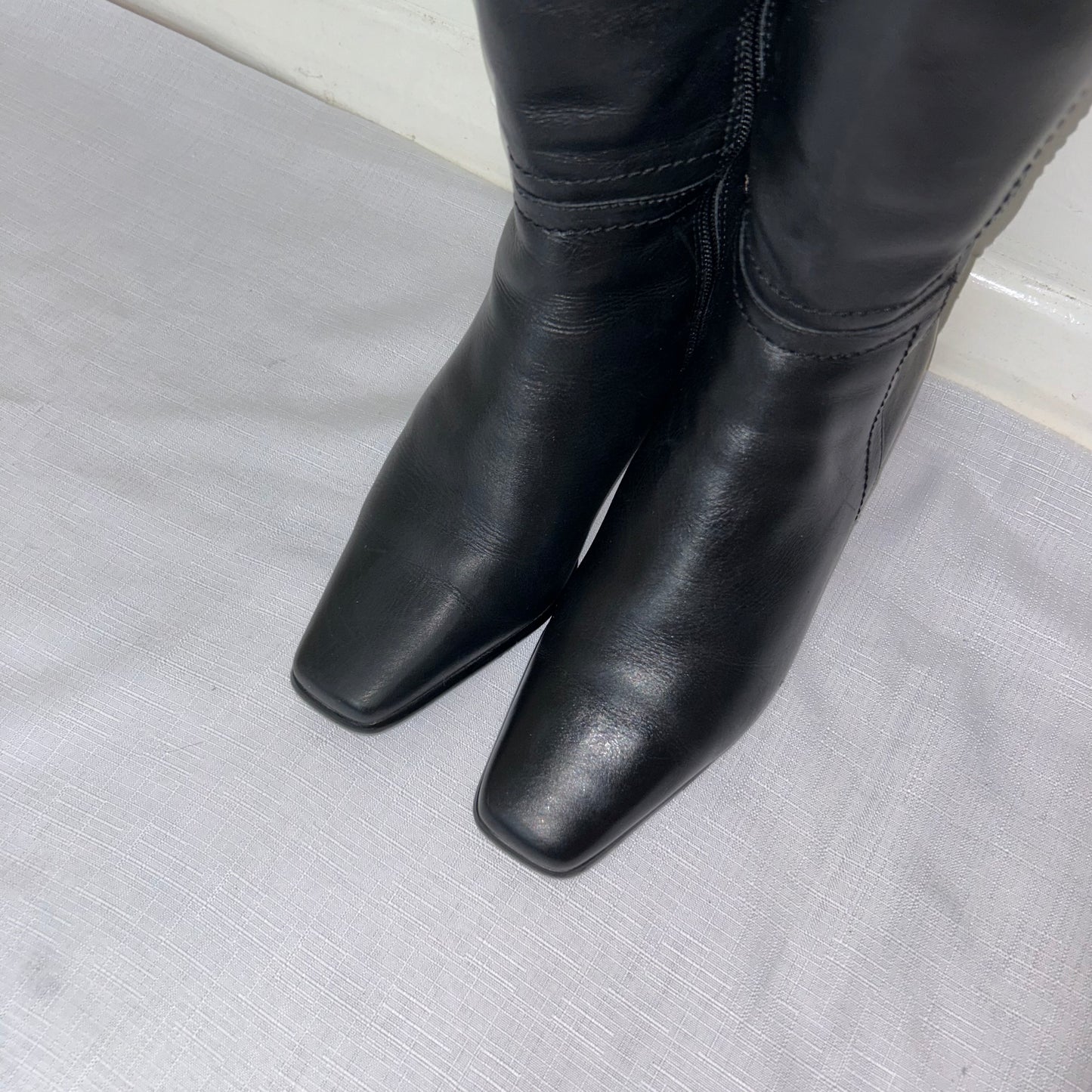 toes of black knee high leather boots shown on a white background