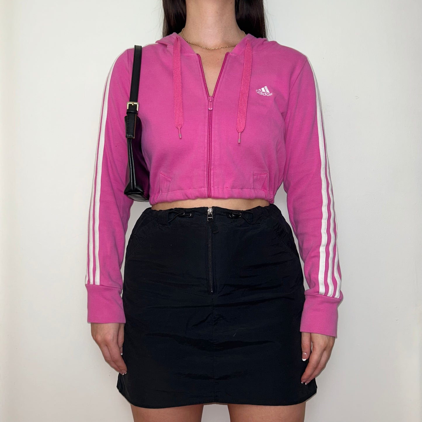 pink zip up hoodie with white adidas logo shown on a model wearing a black mini skirt and black shoulder bag