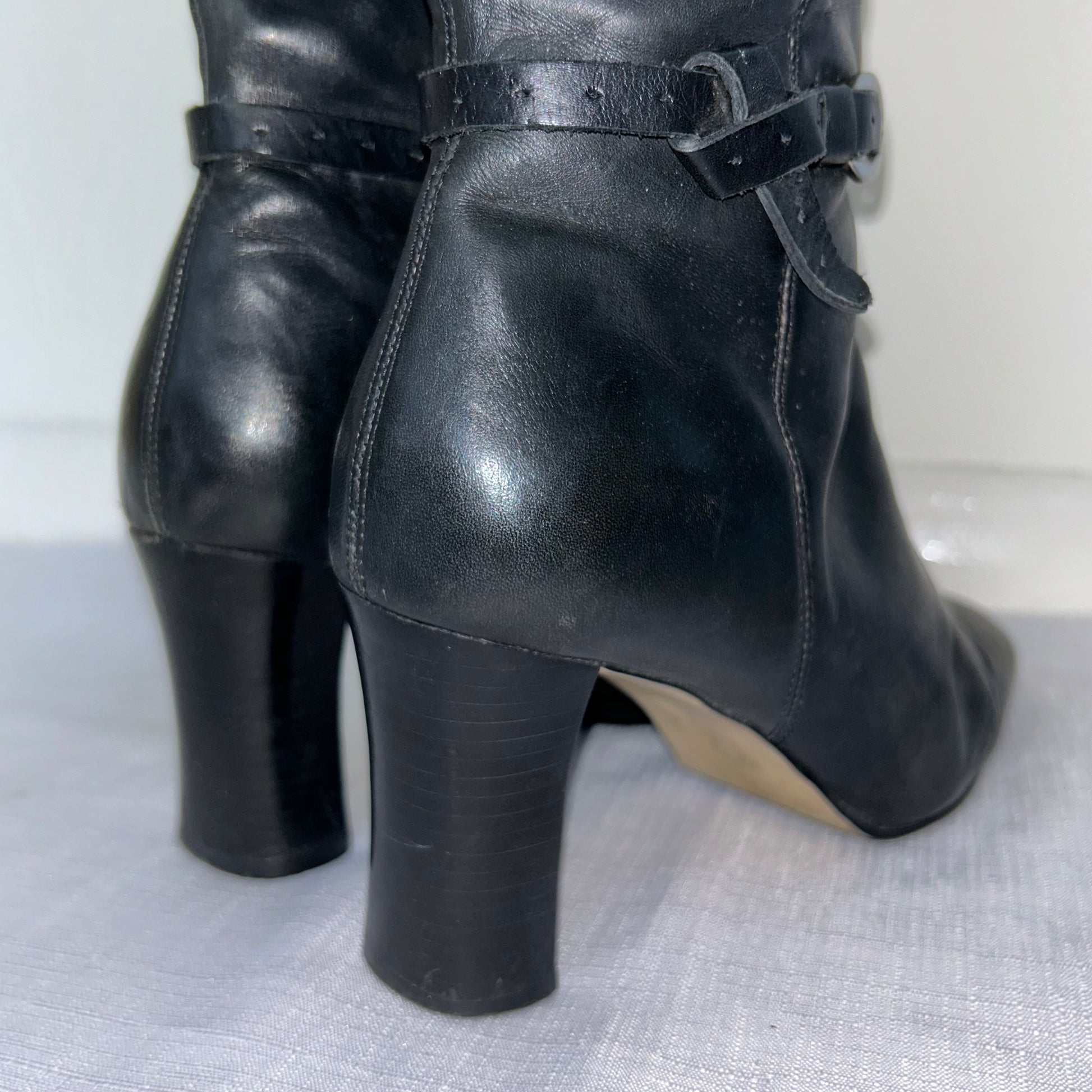 heels of black knee high leather buckle boots on a white background