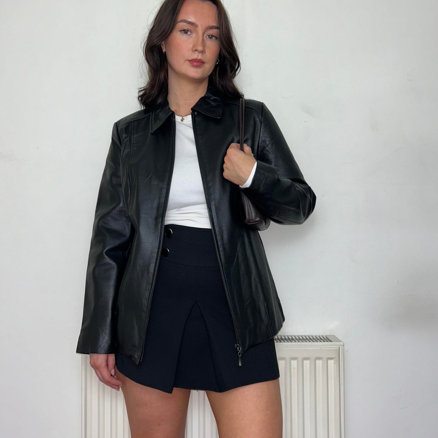 model wearing a black leather bomber jacket with a white top and black skirt with a brown  bag