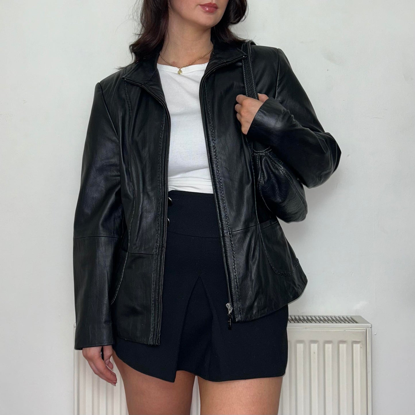 close up of black leather vintage bomber jacket shown on a model wearing a white top and black mini skirt