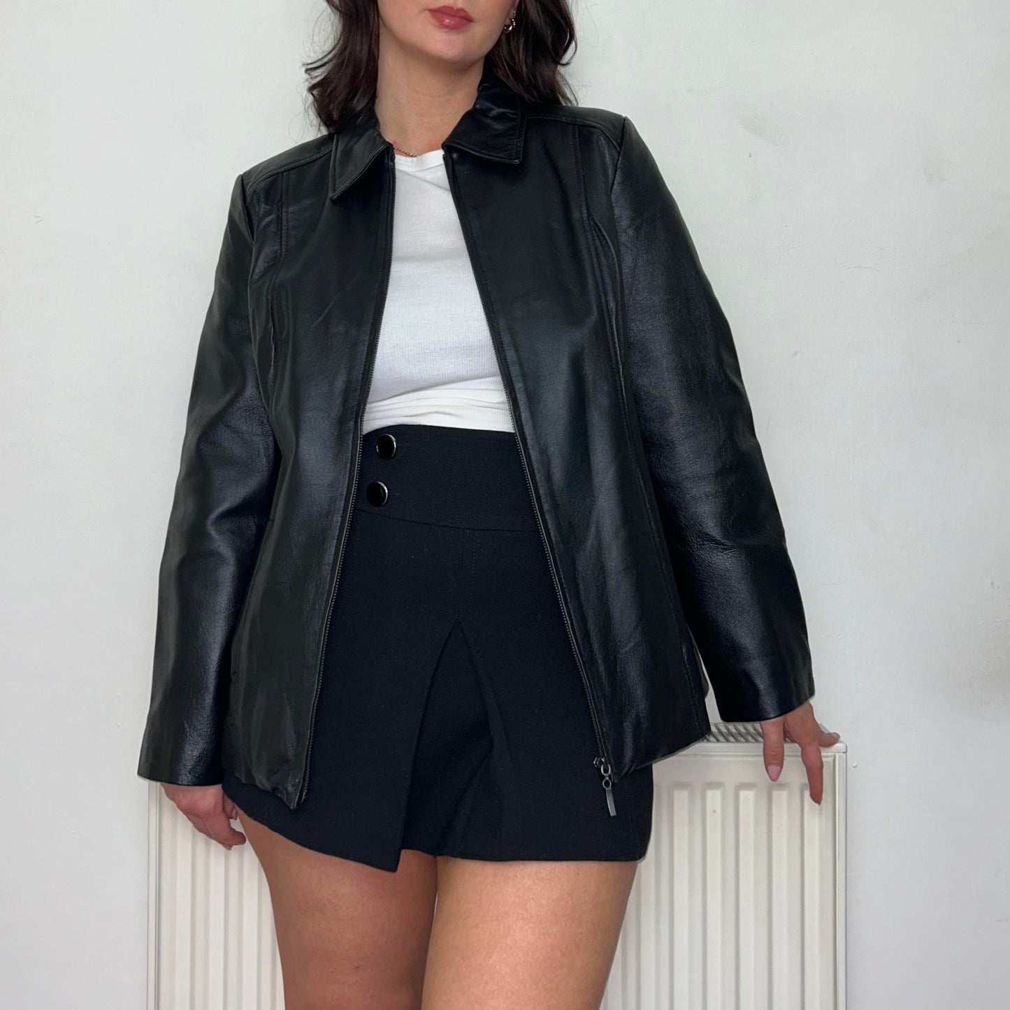 close up of model wearing a black leather bomber jacket with a white top and black skirt