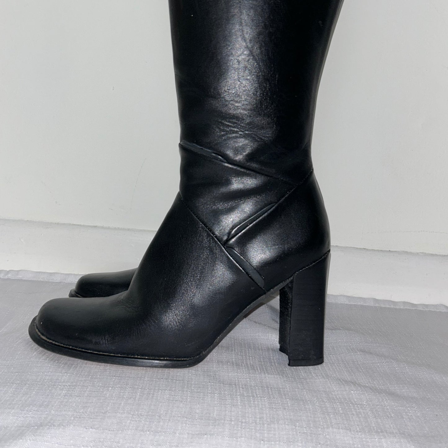 close up of black knee high leather boots shown on a white background