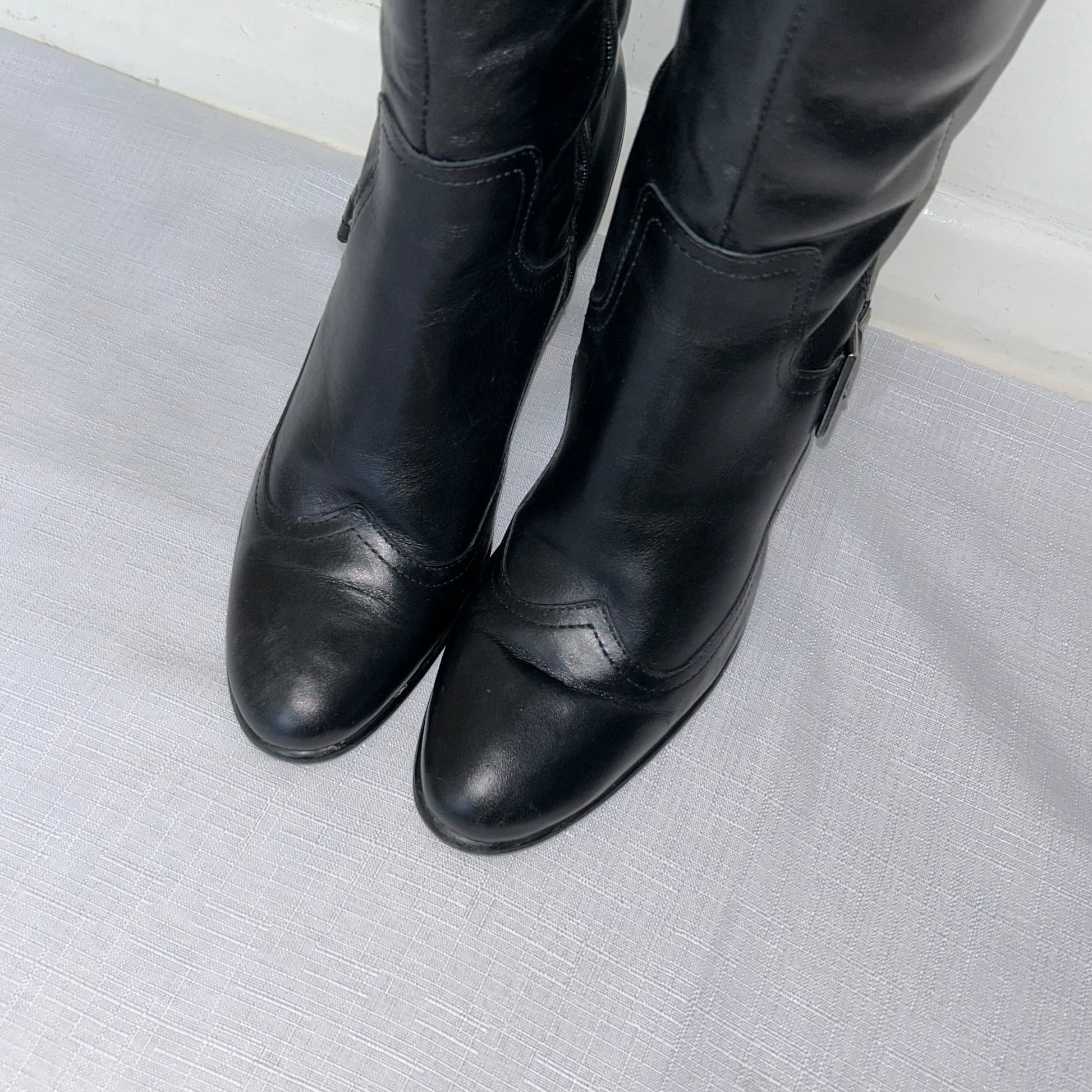 toes of black knee high block heel leather boots shown on a white background