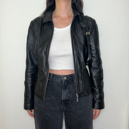 black leather bomber jacket shown on a model wearing a white crop top and black jeans with a black shoulder bag