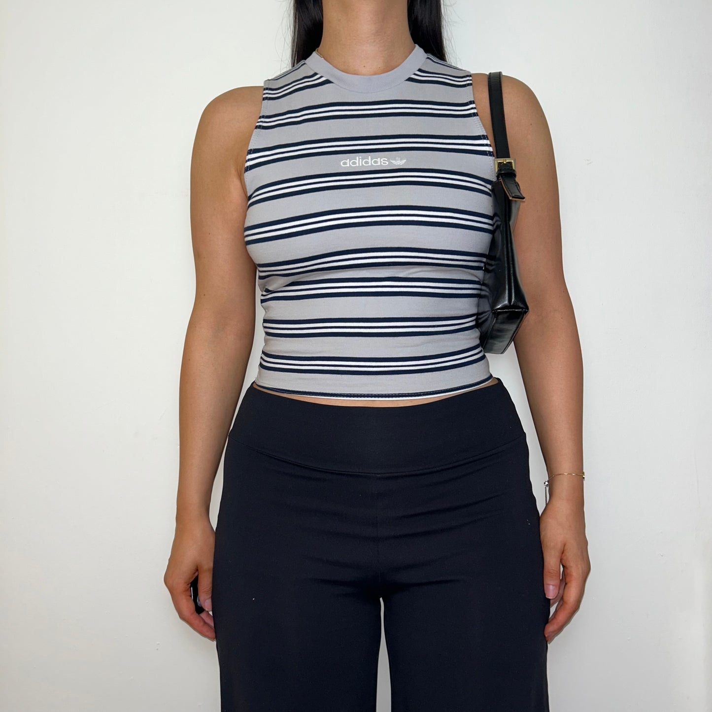 grey stripe sleeveless crop top with white adidas logo shown on a model wearing black trousers and a black shoulder bag