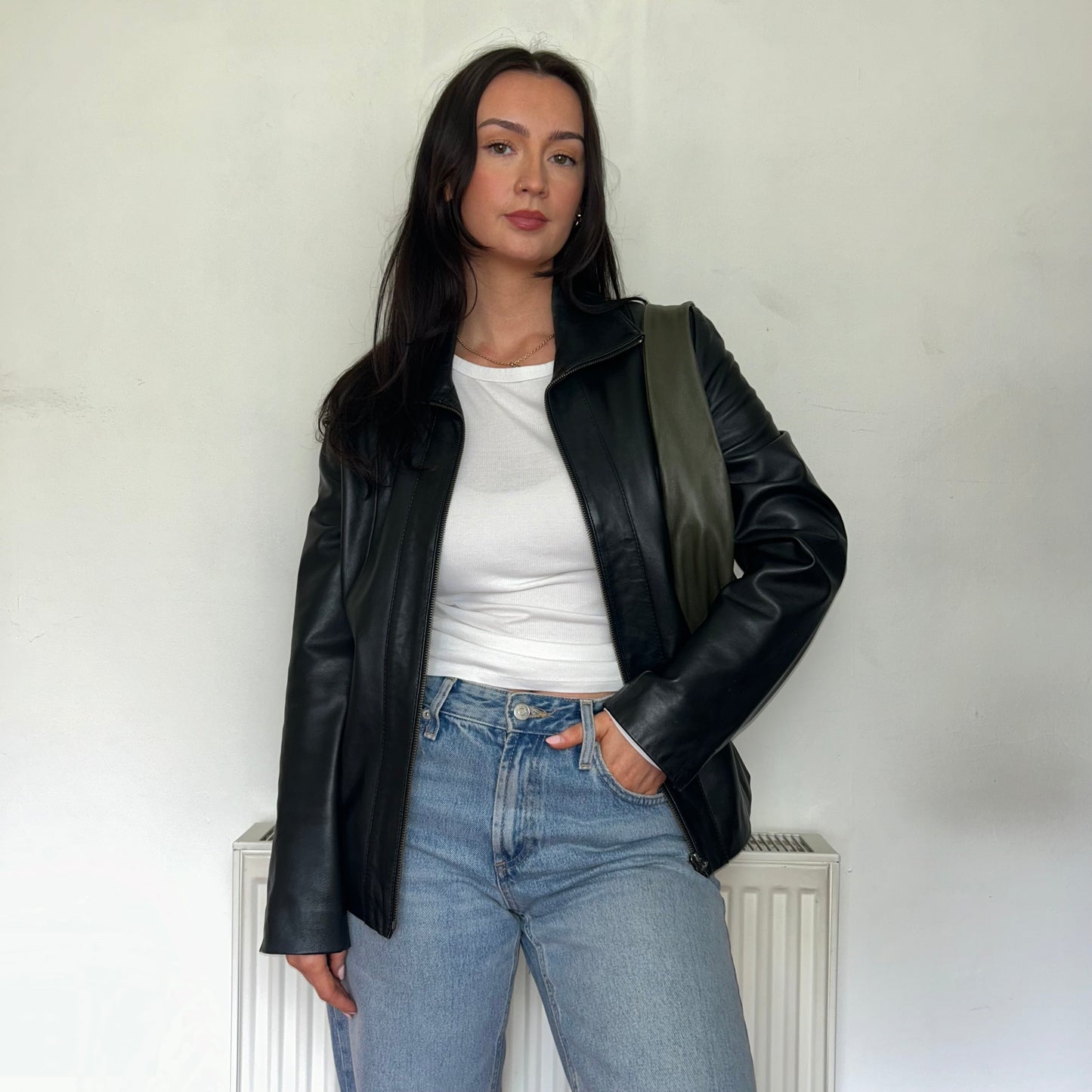 black leather bomber jacket shown on a model wearing a white top and blue jeans with a green bag