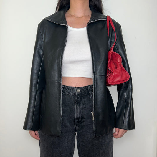 black zip up leather jacket shown on a model wearing a white crop top and black jeans with a red shoulder bag