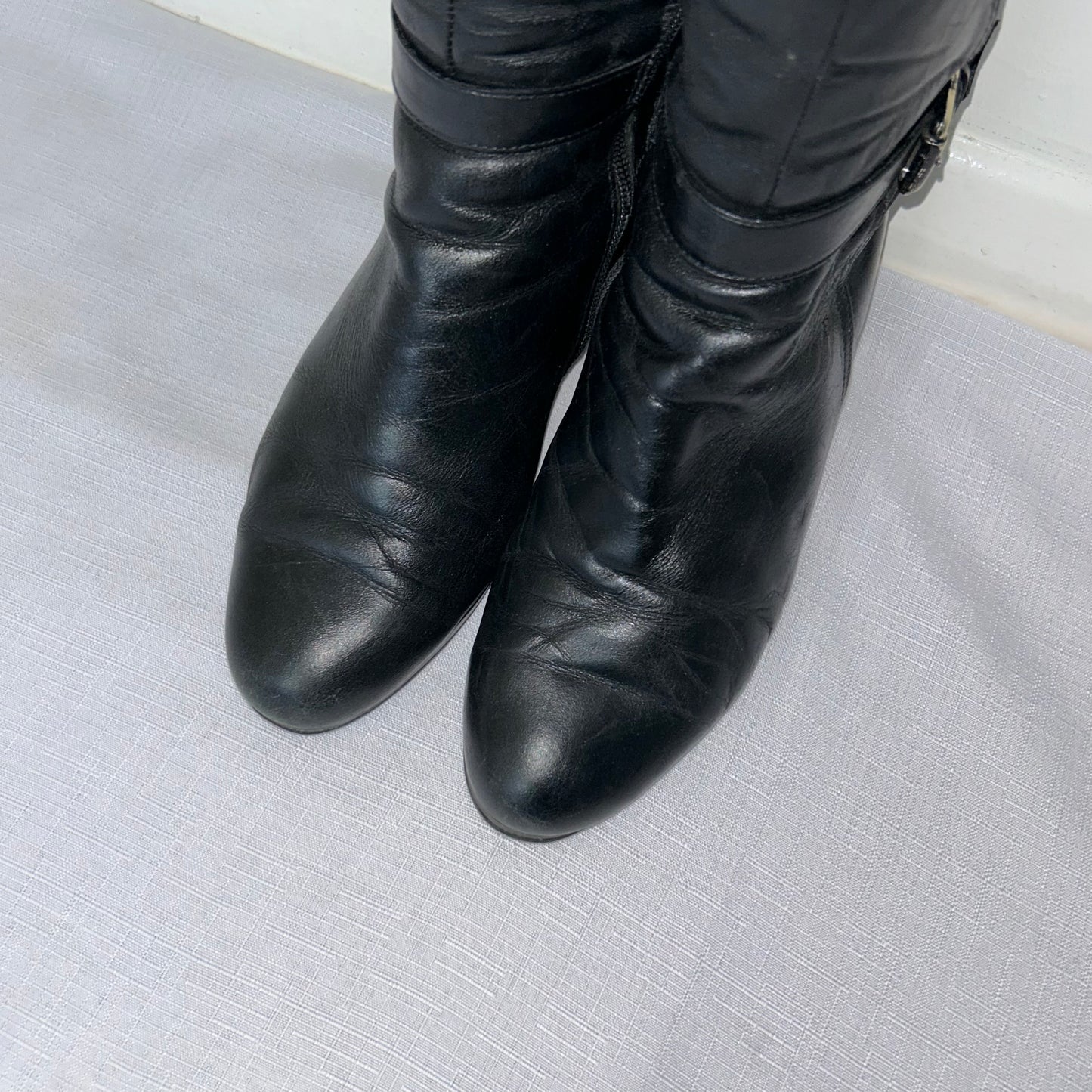 toes of black knee high silver buckle boots shown on a white background
