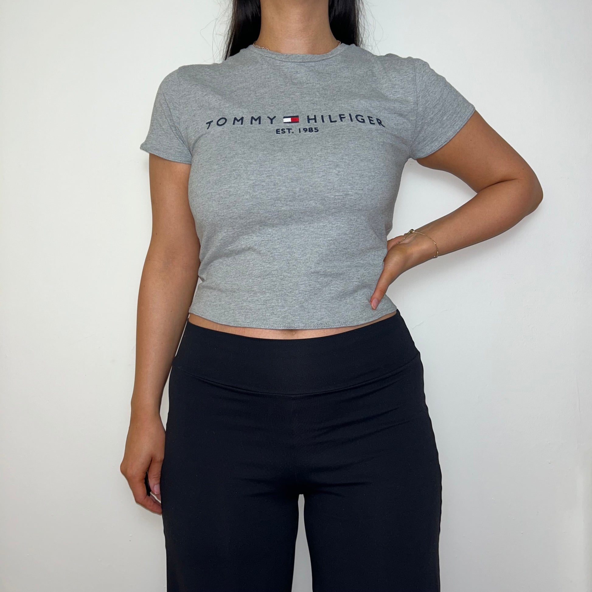 grey short sleeve crop top with black tommy hilfiger logo shown on a model wearing black trousers