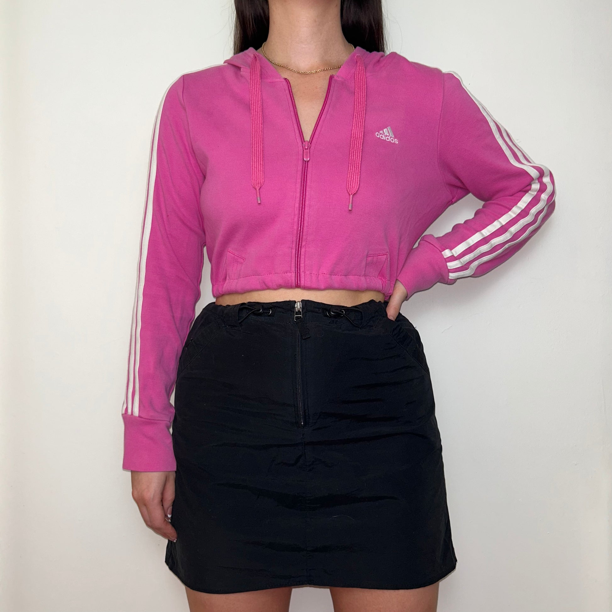 pink zip up hoodie with white adidas logo shown on a model wearing a black mini skirt