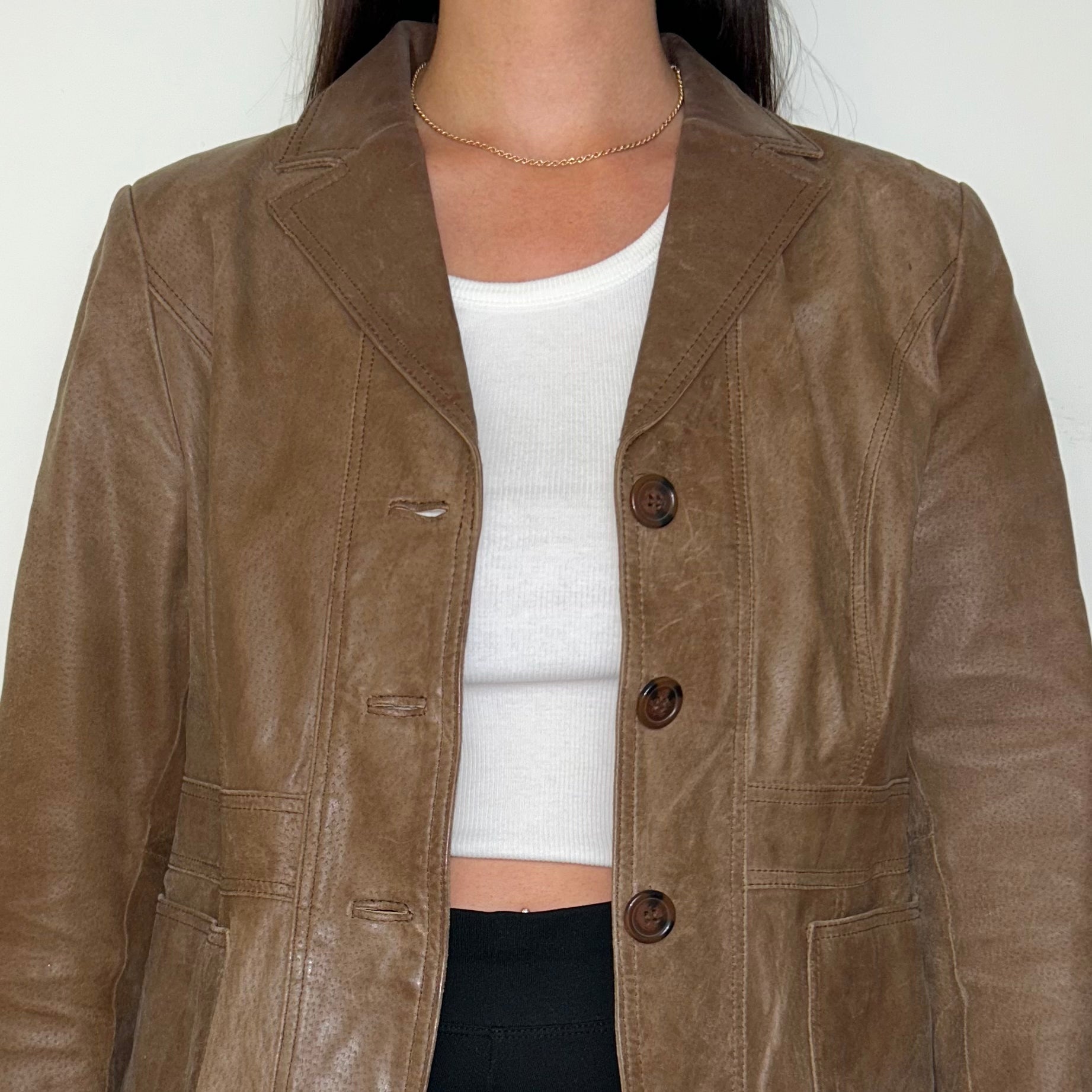 close up of brown leather blazer jacket shown on a model wearing a white crop top and black trousers