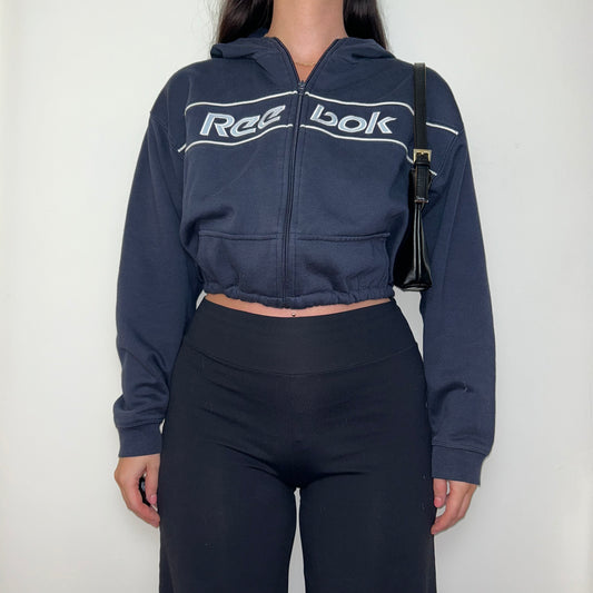navy cropped hoodie with white reebok logo shown on a model wearing black trousers and a black shoulder bag
