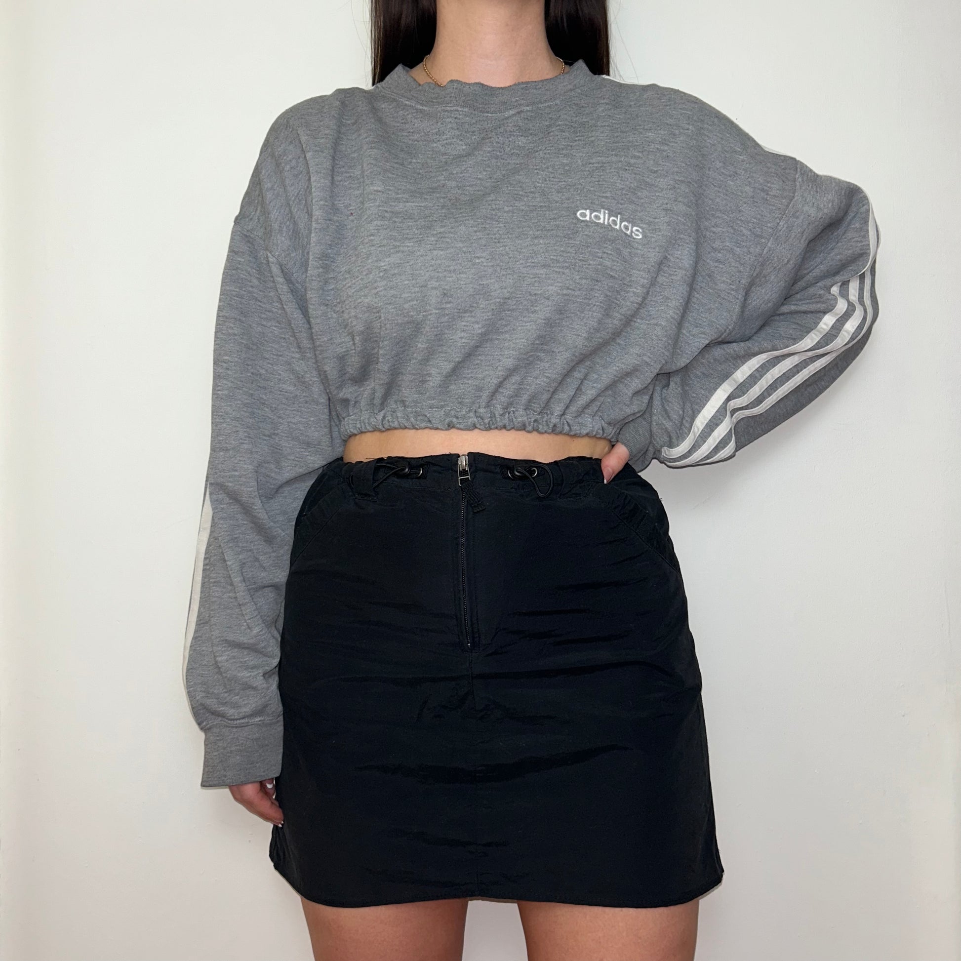grey cropped sweatshirt with white adidas logo shown on a model wearing a black mini skirt