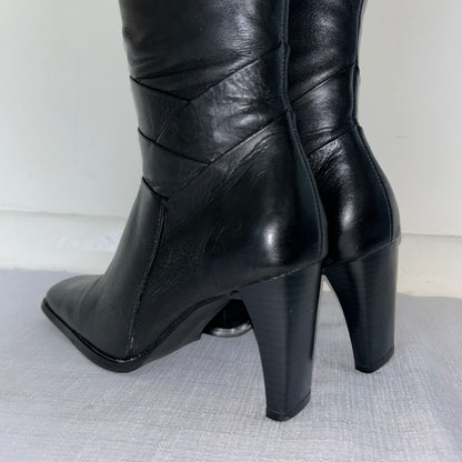 heels of black knee high leather boots on a white background