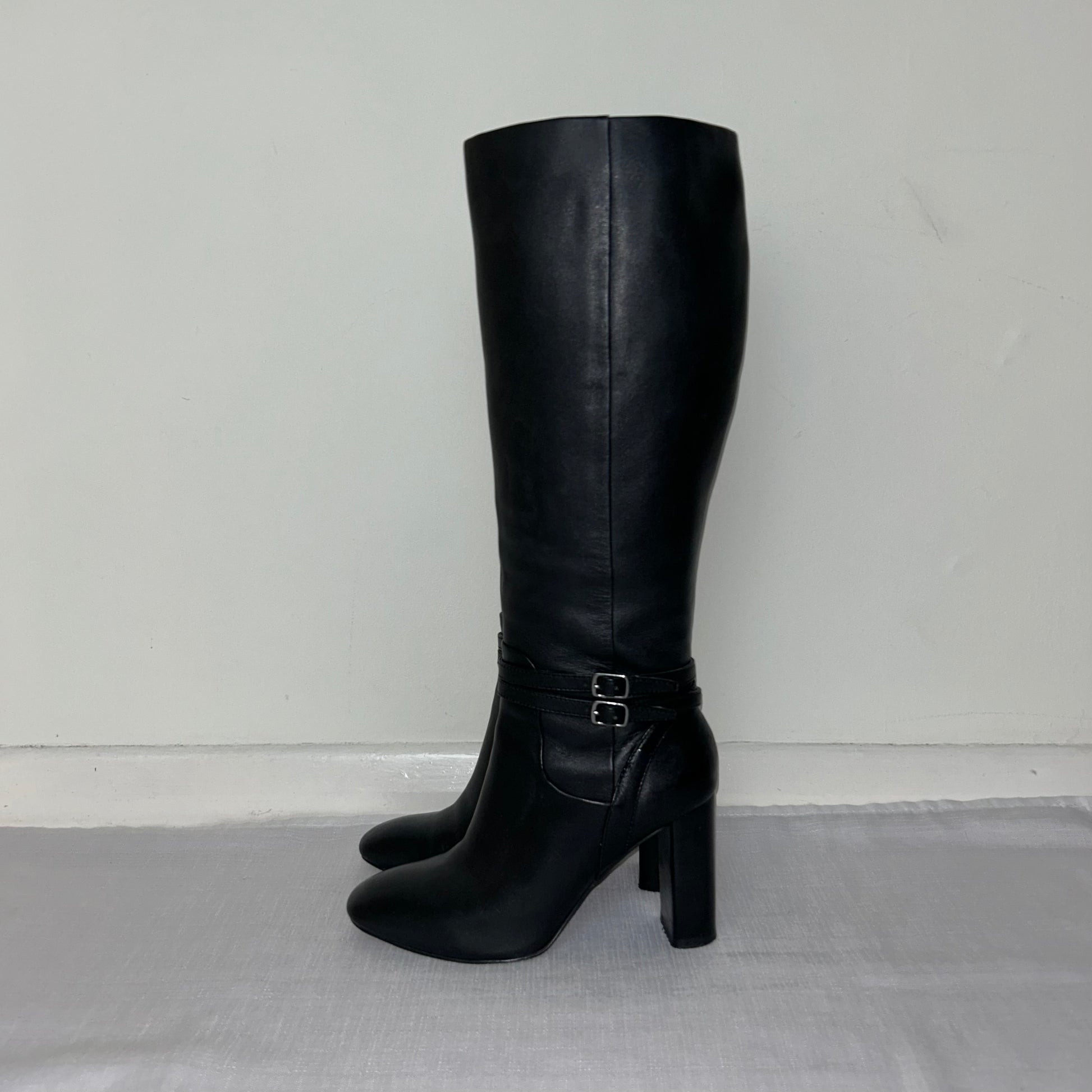 black knee high boots with double silver buckle shown on a white background