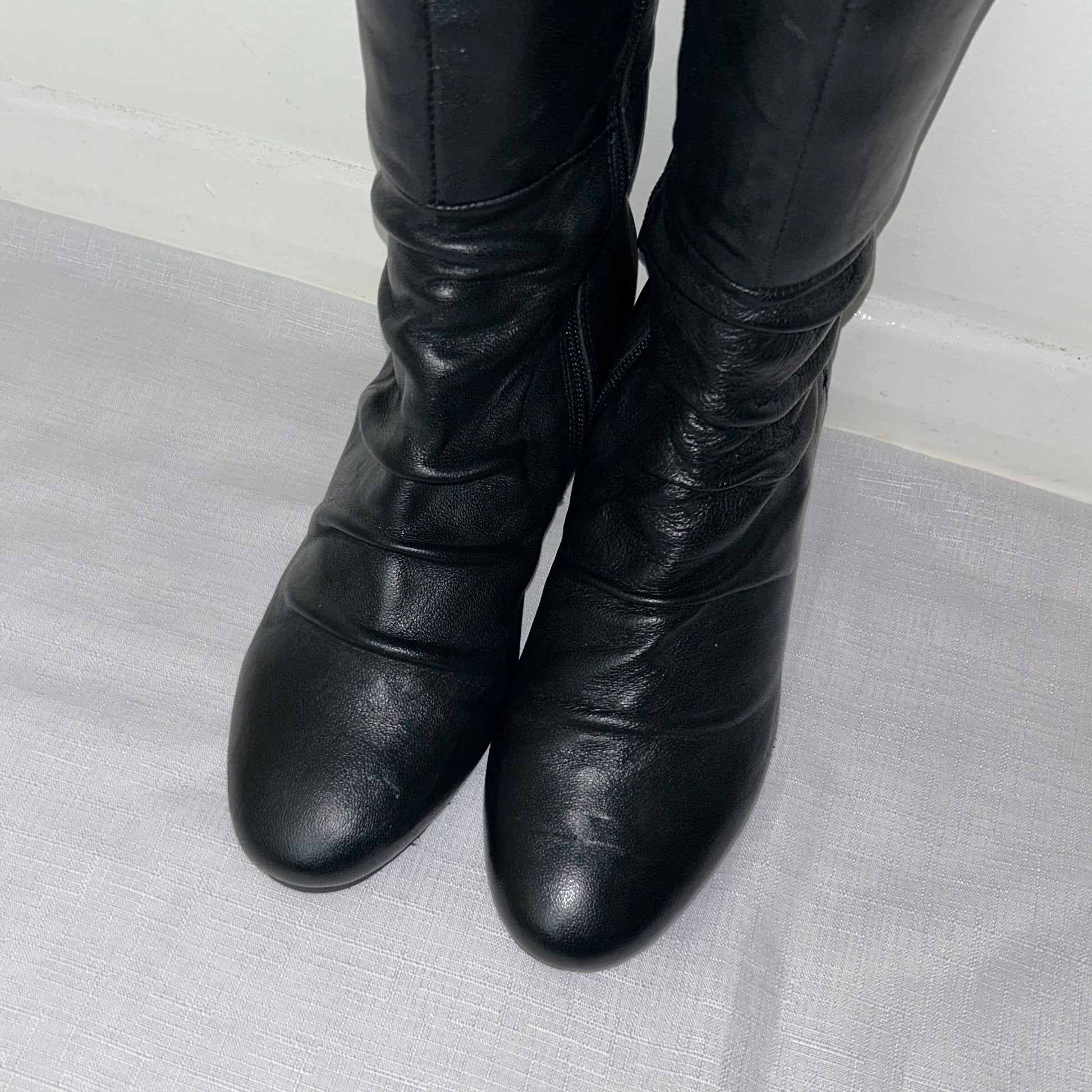 toes of black knee high real leather boots shown on a white background