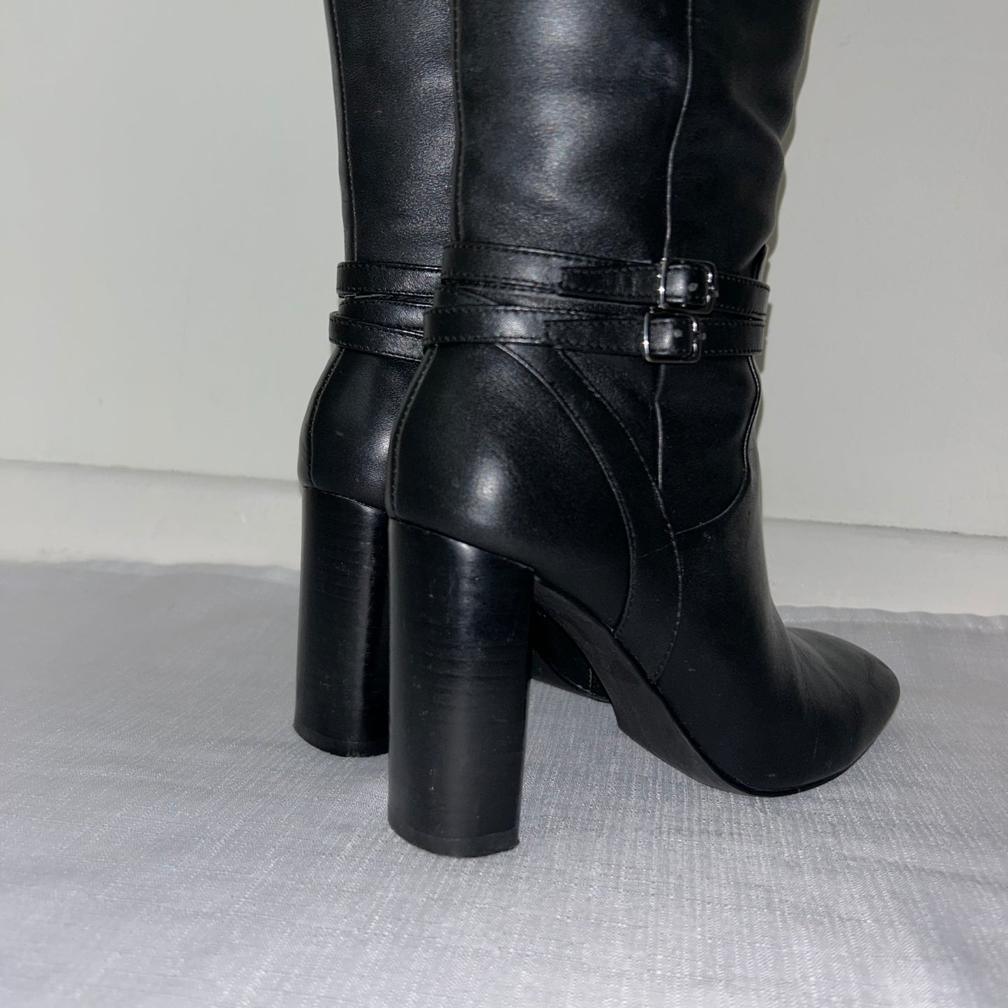 heels of black knee high boots with double silver buckle shown on a white background