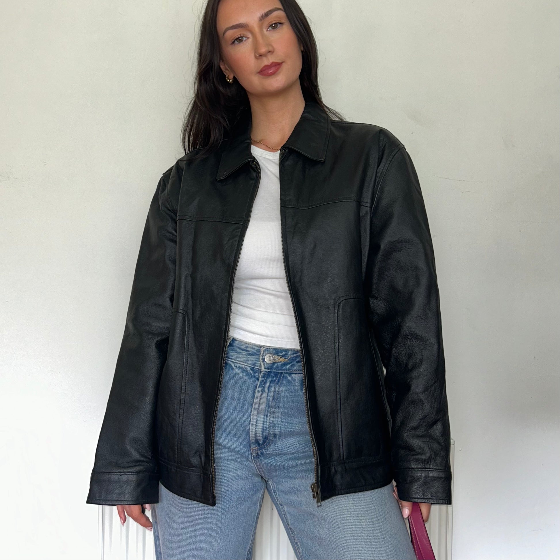 close up of black leather vintage bomber jacket shown on a model wearing a white top and blue jeans
