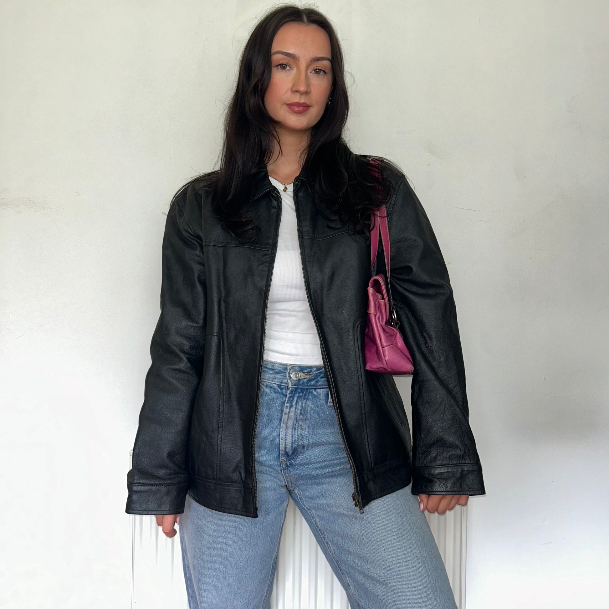 black leather vintage bomber jacket shown on a model wearing a white top and blue jeans with a pink bag