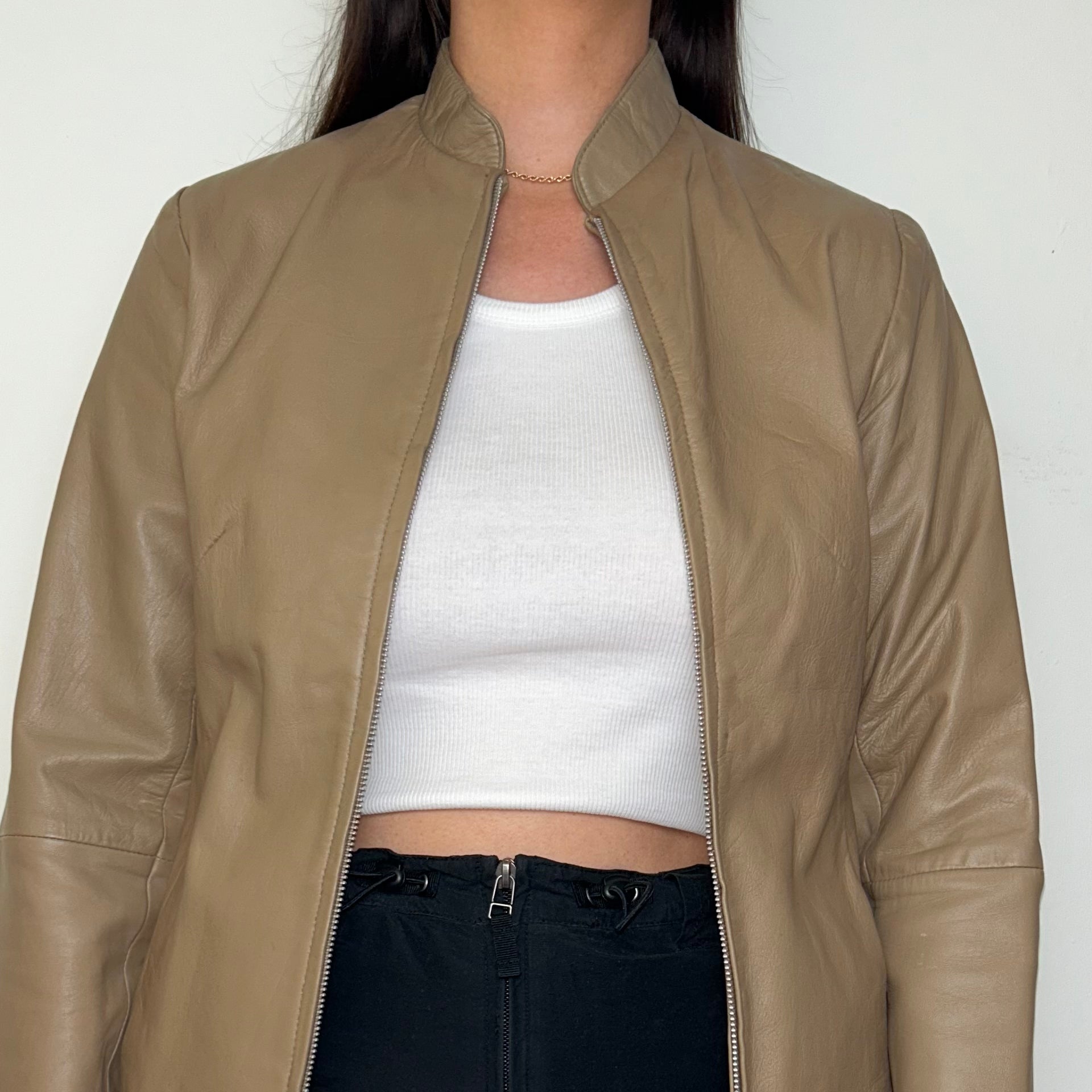 close up of tan beige real leather jacket shown on a model wearing a white crop top and black mini skirt