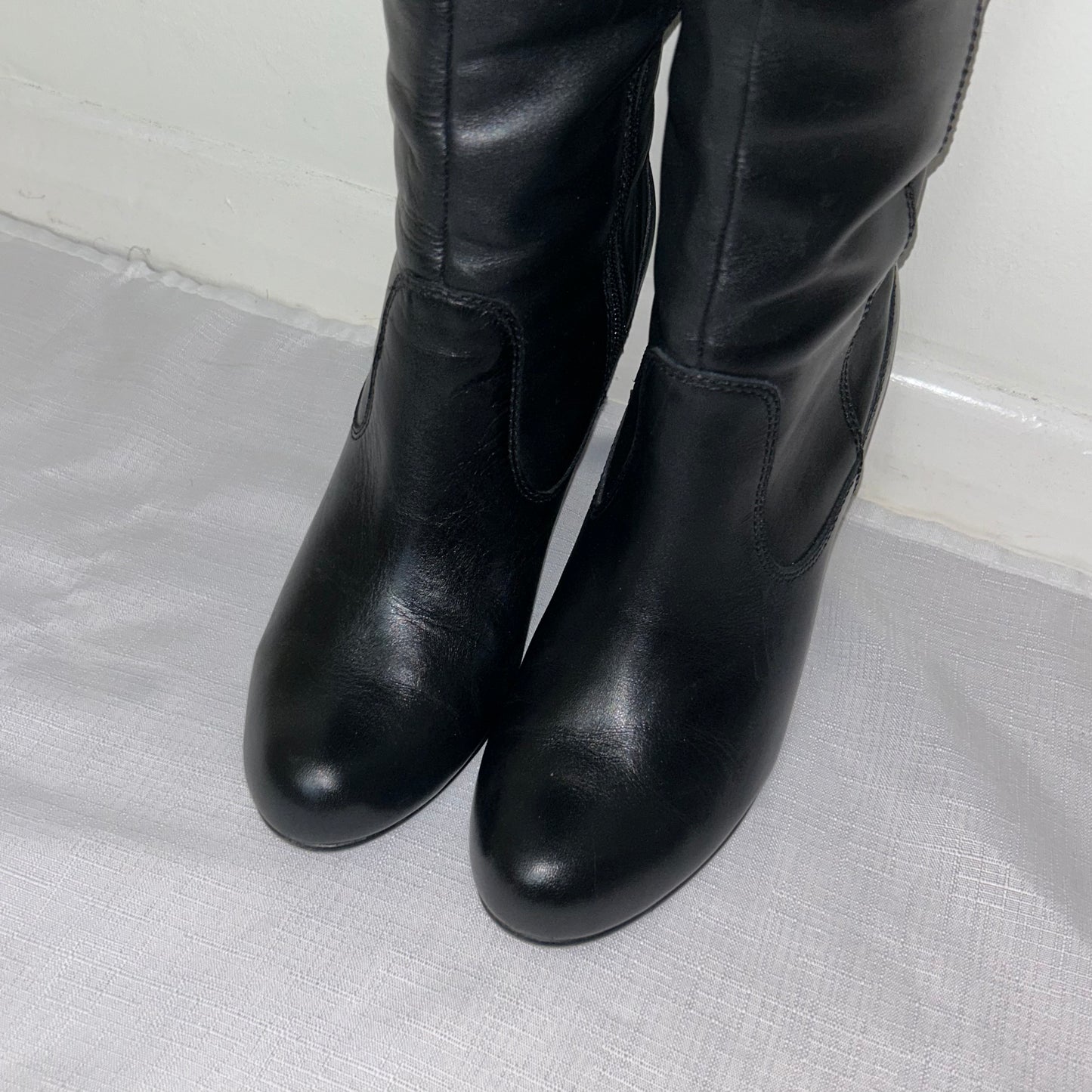 toes of black knee high real leather boots on a white background