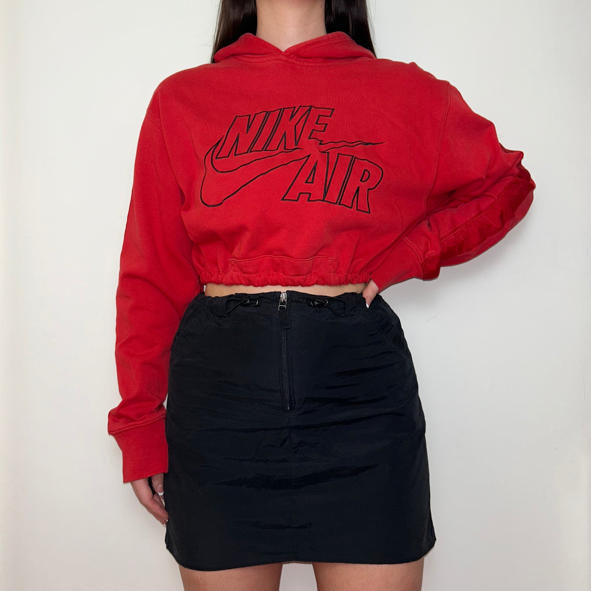 red cropped hoodie with black nike air logo shown on a model wearing a black mini skirt