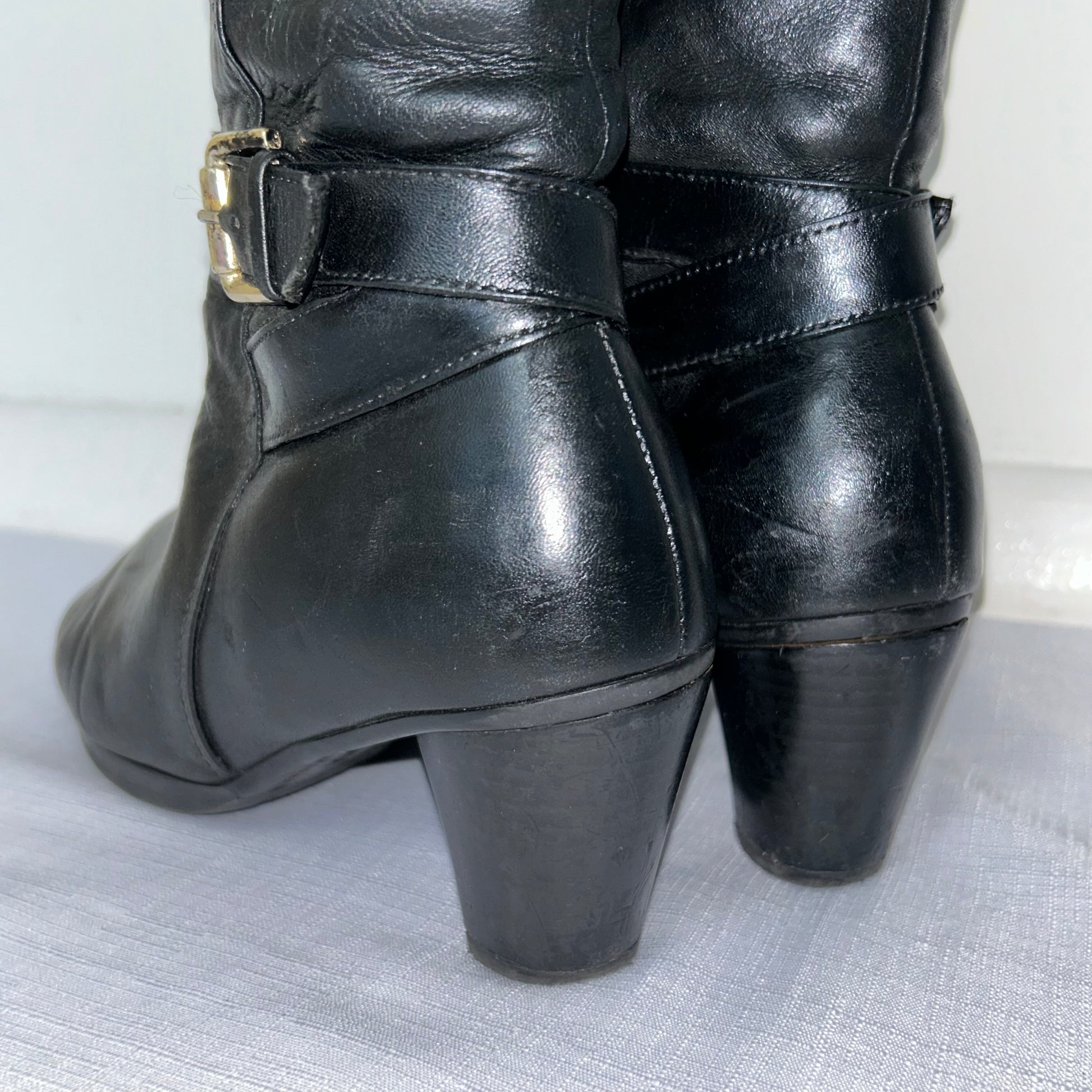 heels of black knee high silver buckle boots shown on a white background