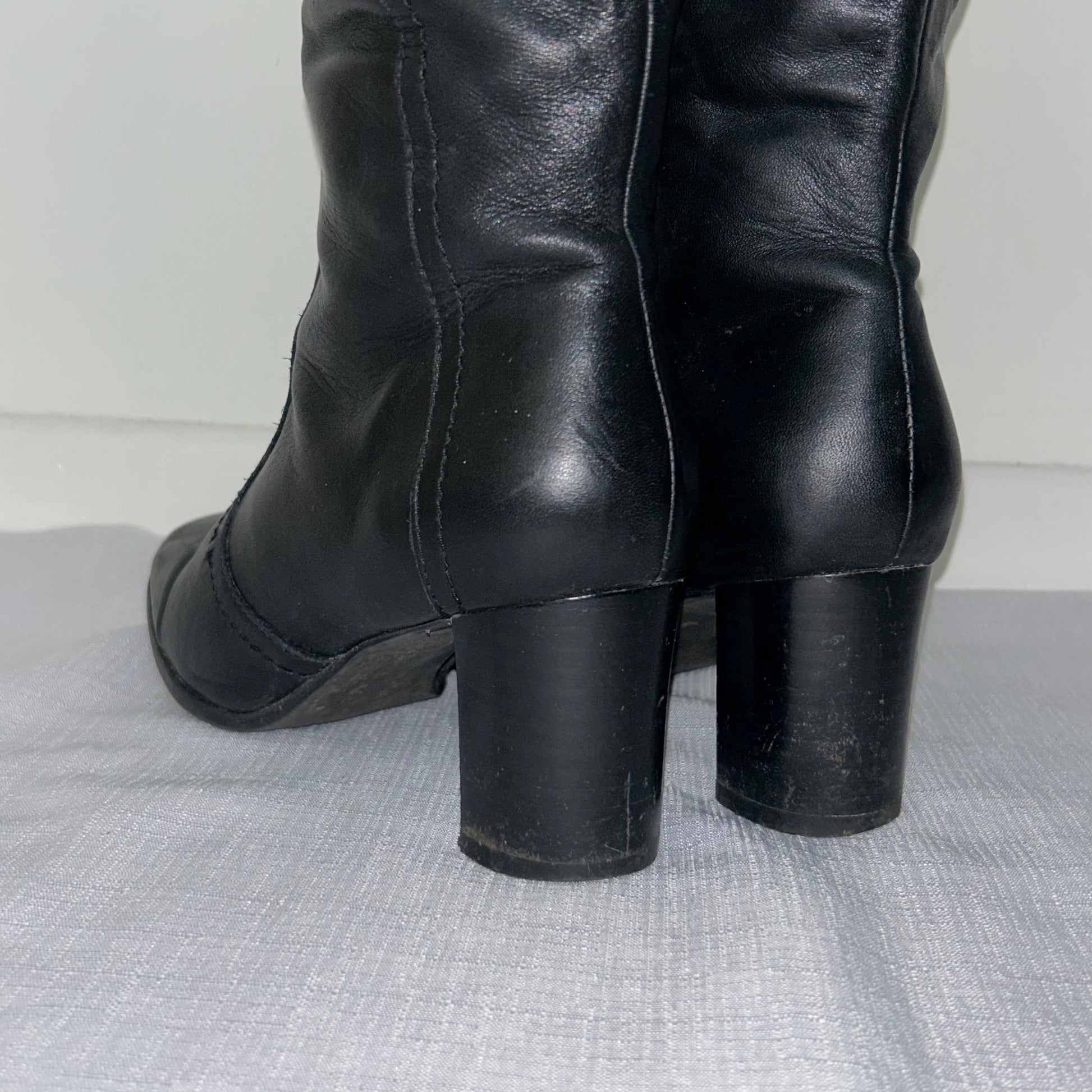 heels of black knee high real leather boots shown on a white background