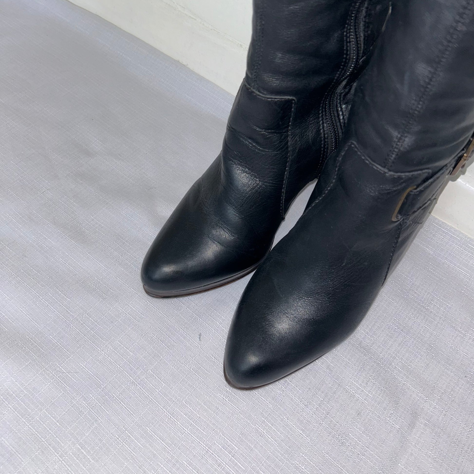 toes of black knee high buckle boots shown on a white background